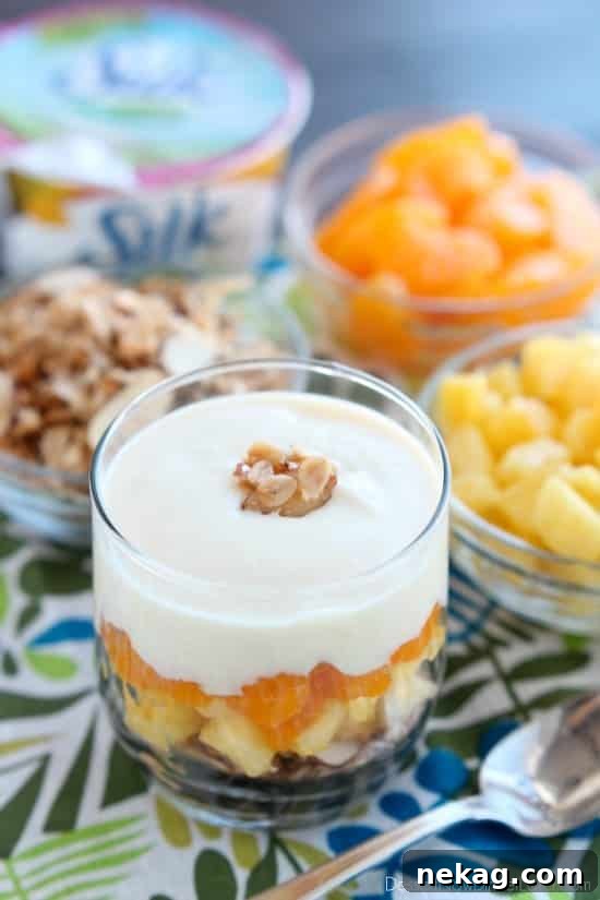 A hand holding a glass of the freshly prepared Dairy-Free Tropical Parfait, ready to be enjoyed, with a spoon digging into the vibrant layers.