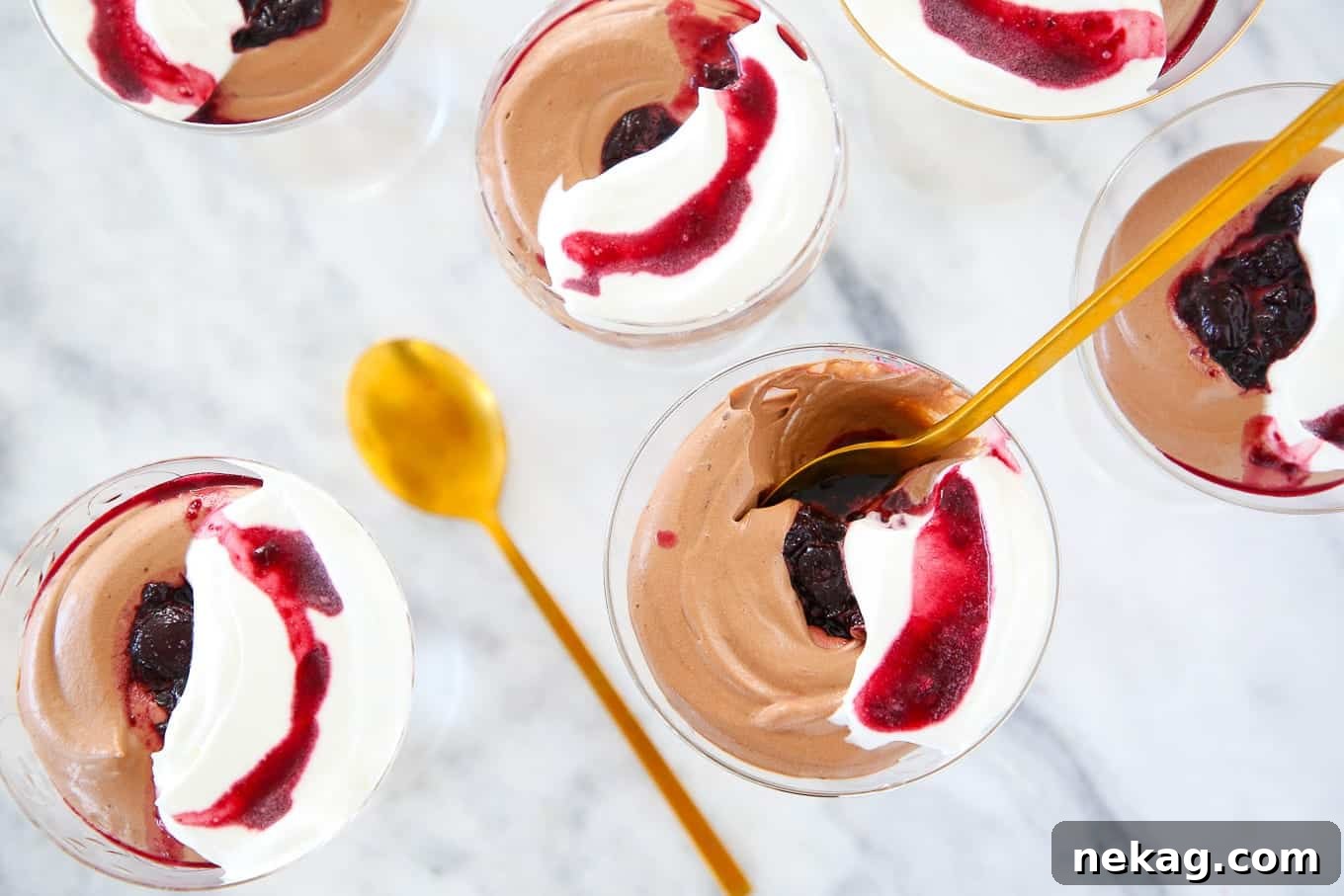 Decadent Chocolate Mousse 3 Two glasses of chocolate mousse with cherry swirl on a white marble surface, garnished with fresh cherries.
