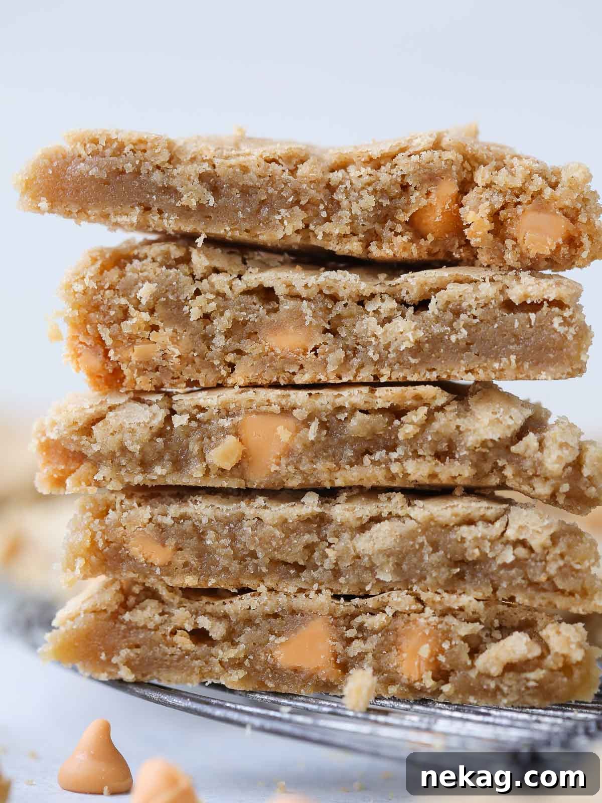 Five golden, chewy blondies stacked high on a wooden surface, showcasing their delicious texture and inviting color.