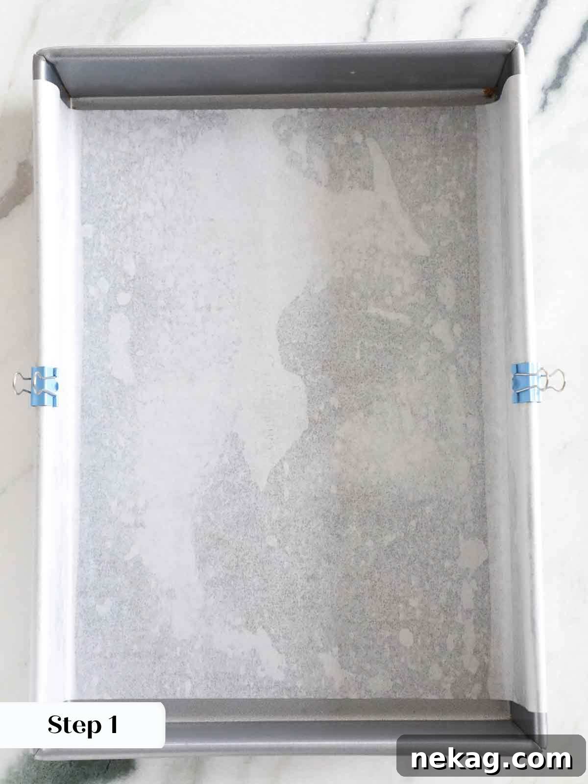 A 9x13 inch metal baking pan, perfectly lined with crisscrossed parchment paper, ready for blondie batter.
