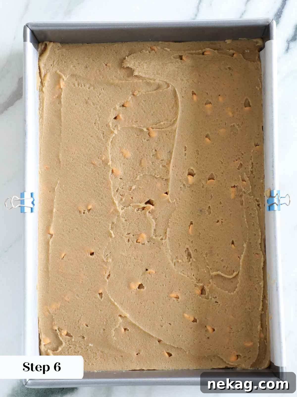 An offset spatula smoothly spreading blondie batter evenly into a prepared baking dish, creating a flat surface.