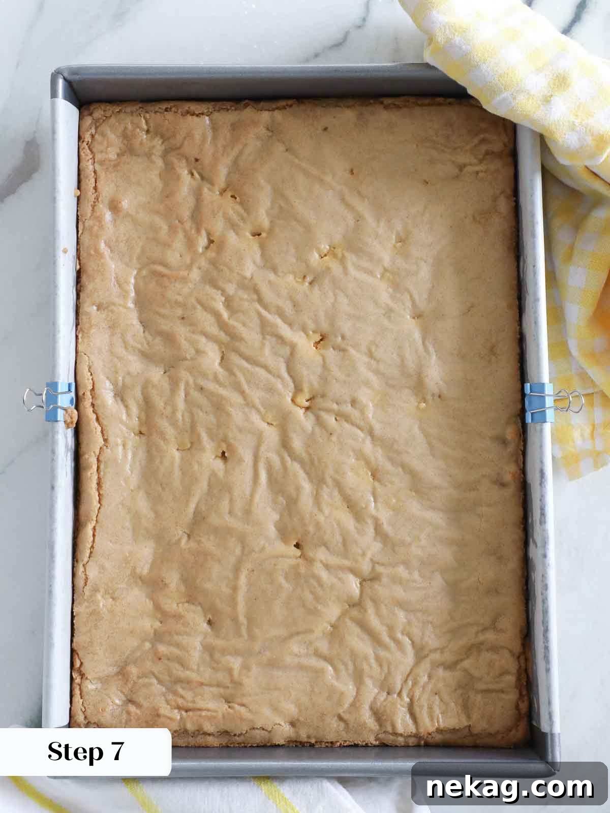 Baked blondies cooling in the metal pan, showing a golden brown top and slightly deflated center, indicating perfect doneness.