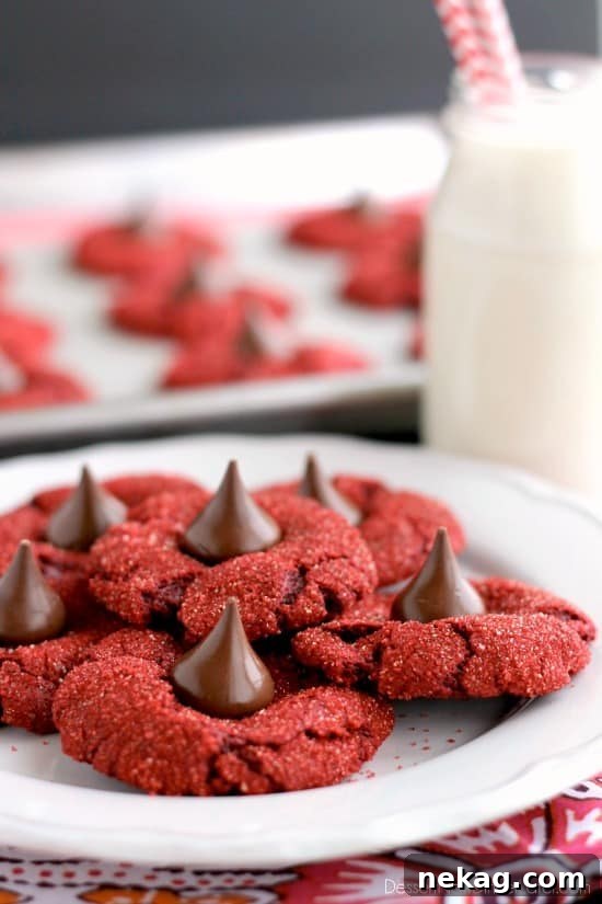 Red Velvet Bloom Cookies 4 Stack of Red Velvet Blossom Cookies on a cooling rack, showcasing their uniform shape and the attractive contrast of red cookie and brown chocolate kiss. The sparkling red sugar is visible on the edges of the cookies.