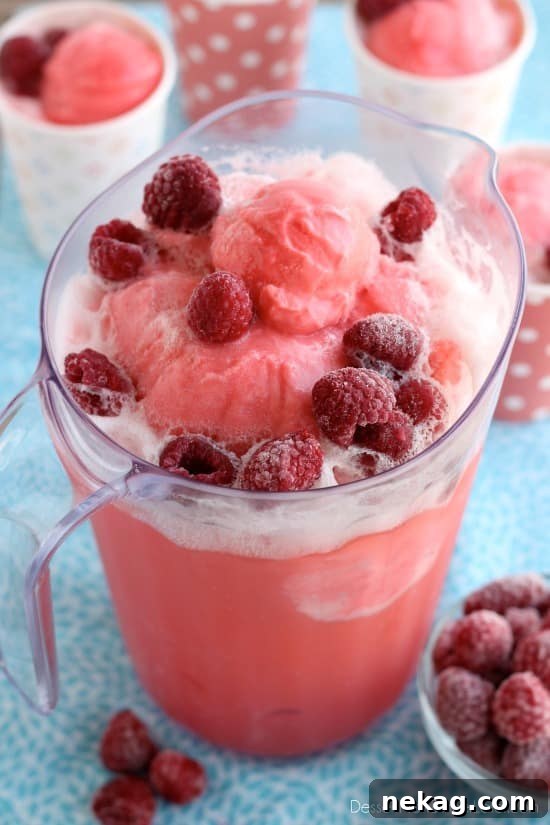 Close-up of pink sherbet punch in a glass with frozen raspberries, highlighting the froth and fizz.