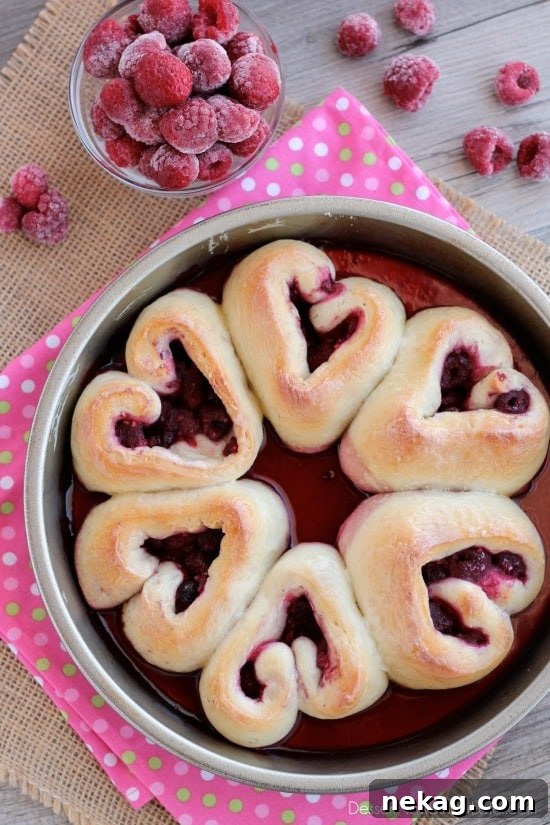 Sweetheart Raspberry Swirls 2 A close-up view of beautifully glazed heart-shaped raspberry rolls nestled in a round cake pan, ready to be enjoyed for a special occasion like Valentine's Day.