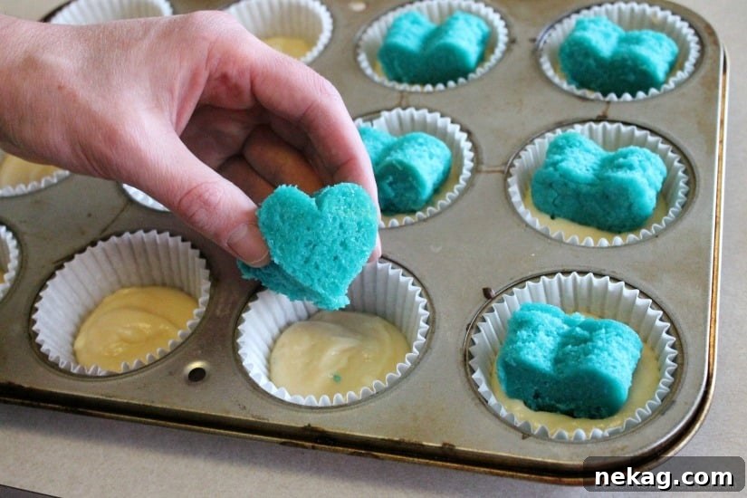 He or She Sweet Bites 7 Cupcake liners filled with white batter, with a blue heart carefully placed in the center of each.