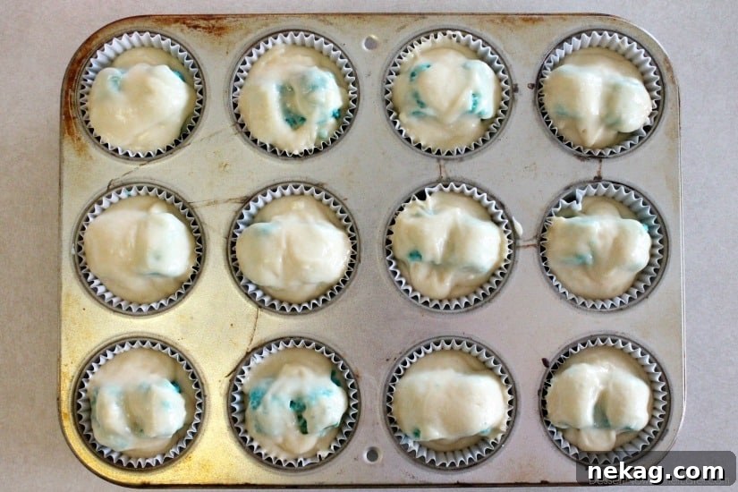 He or She Sweet Bites 8 More white cupcake batter being scooped over the hidden blue hearts before baking.