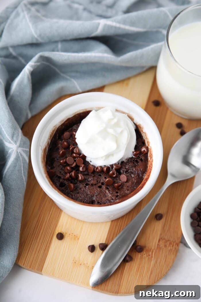 A close-up of a delectable single-serving chocolate cake in a ramekin, generously topped with an array of mini chocolate chips and a delicate swirl of whipped cream, inviting a taste.