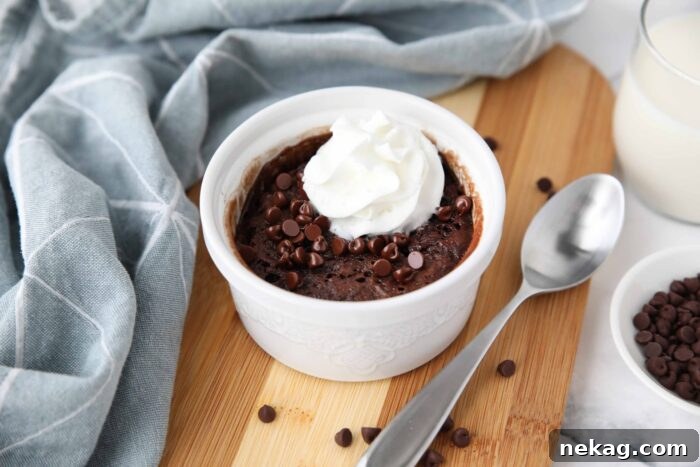 A tempting image of a single-serving chocolate cake in a ramekin, beautifully adorned with melted mini chocolate chips and a swirl of whipped cream, presented invitingly on a wooden surface.