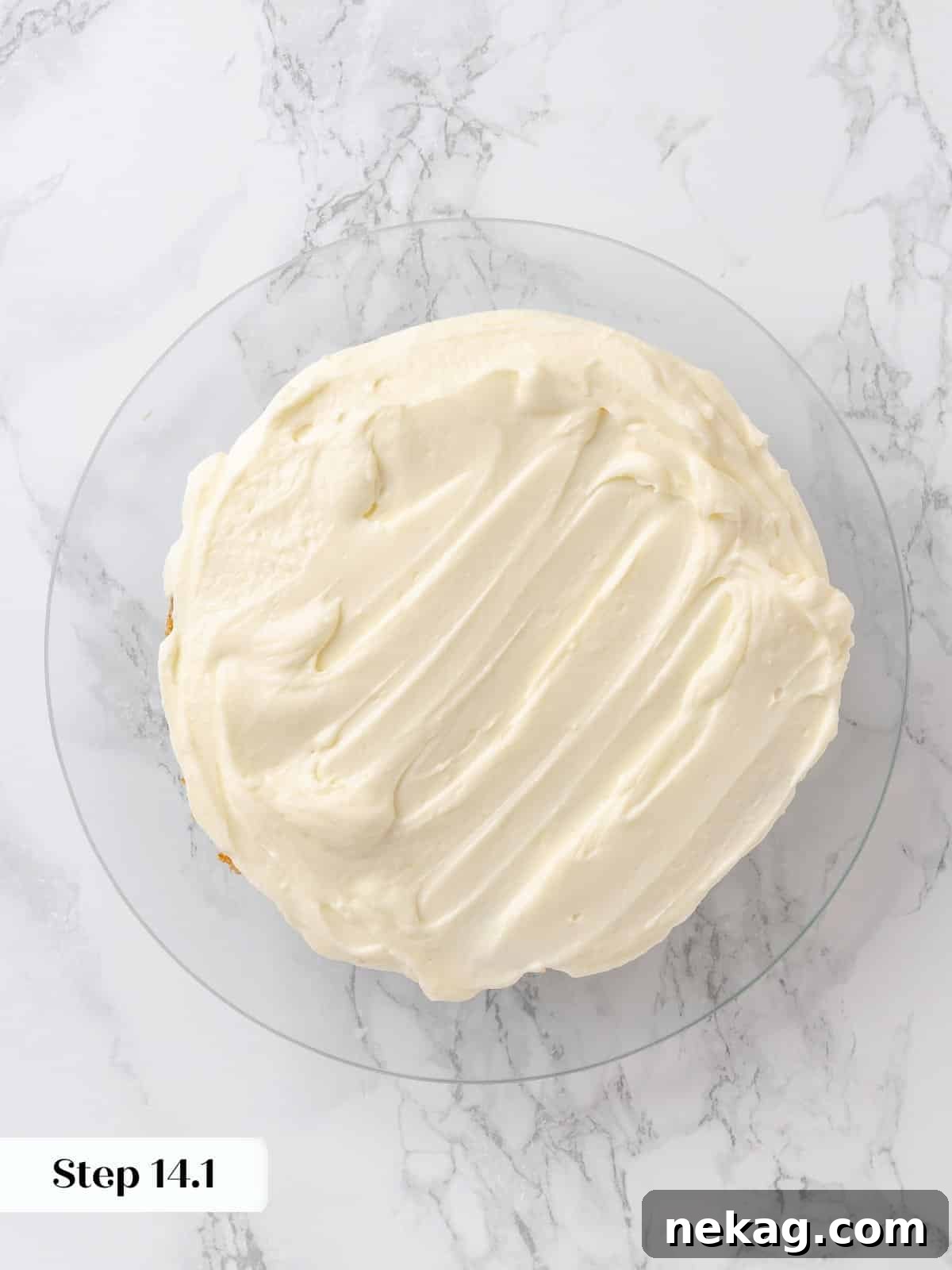 First cake layer covered in a smooth layer of cream cheese frosting.