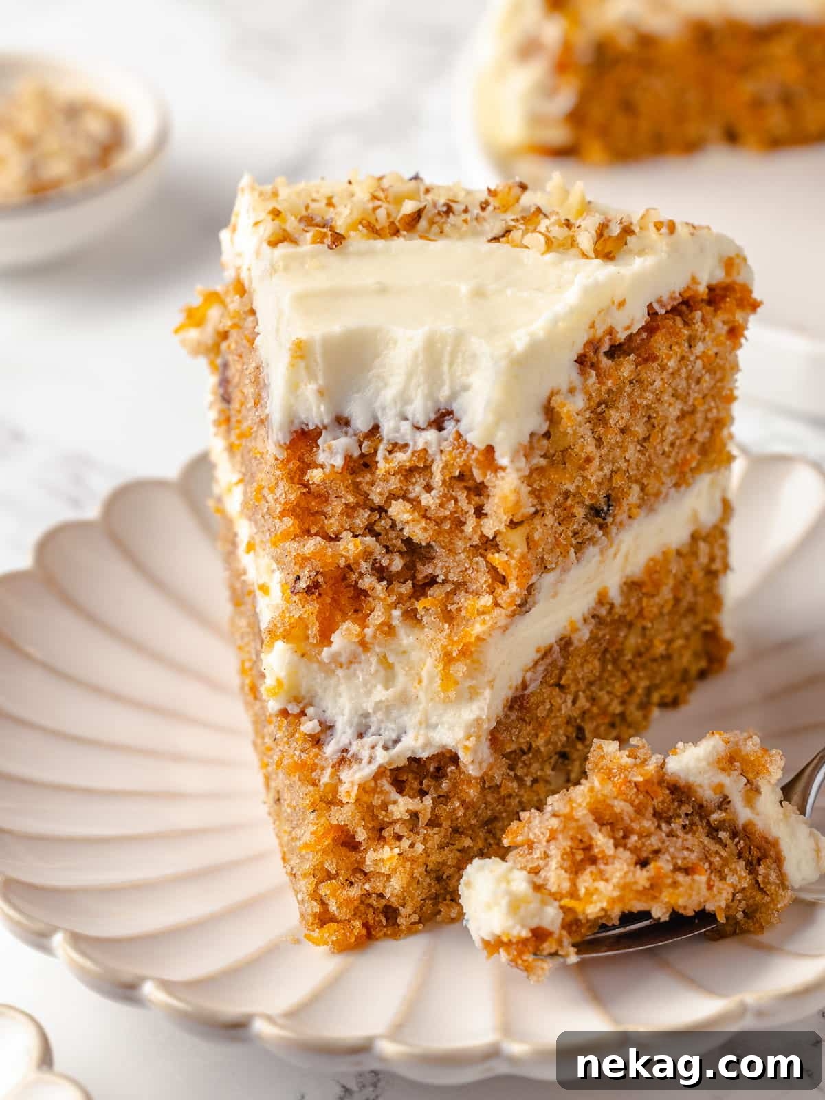 A slice of carrot cake on a plate with a fork, showing a bite taken.
