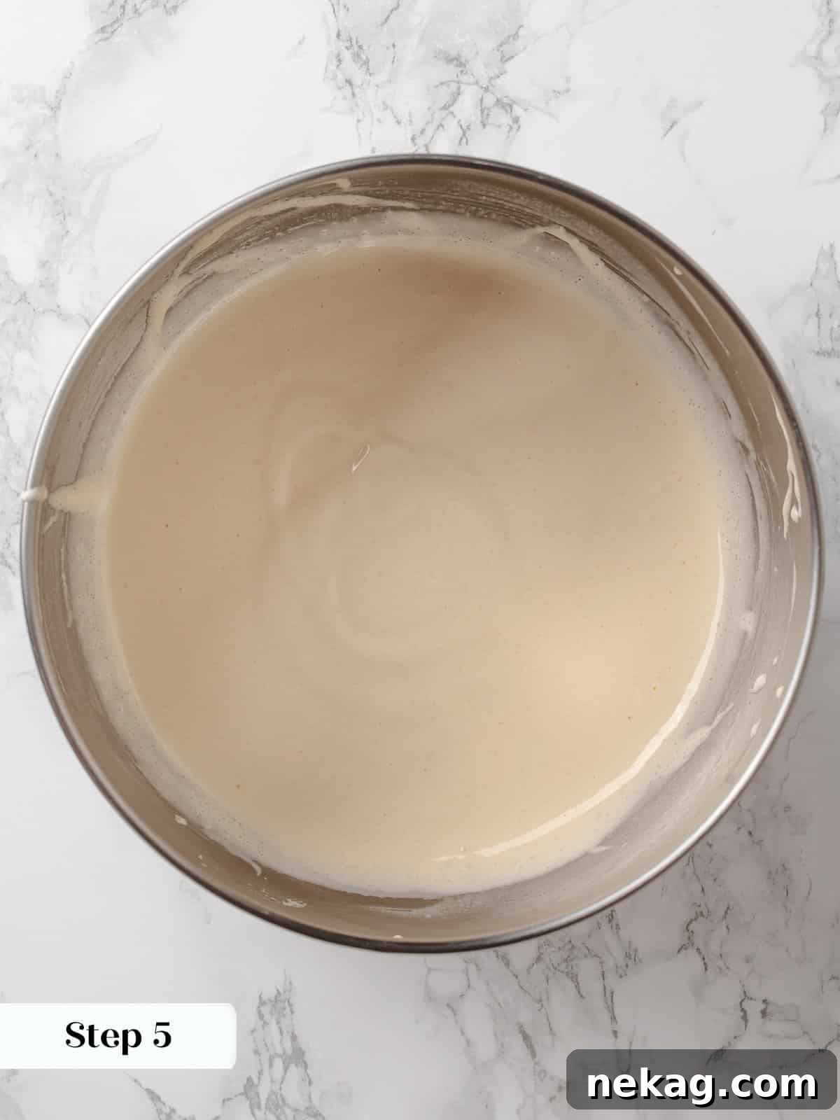 Pale and voluminous egg and sugar mixture in a stand mixer bowl, showing ribbon stage.