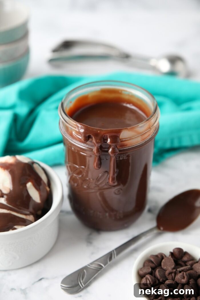 Close-up of rich hot fudge dripping down the side of a glass mason jar, highlighting its thick, glossy consistency.