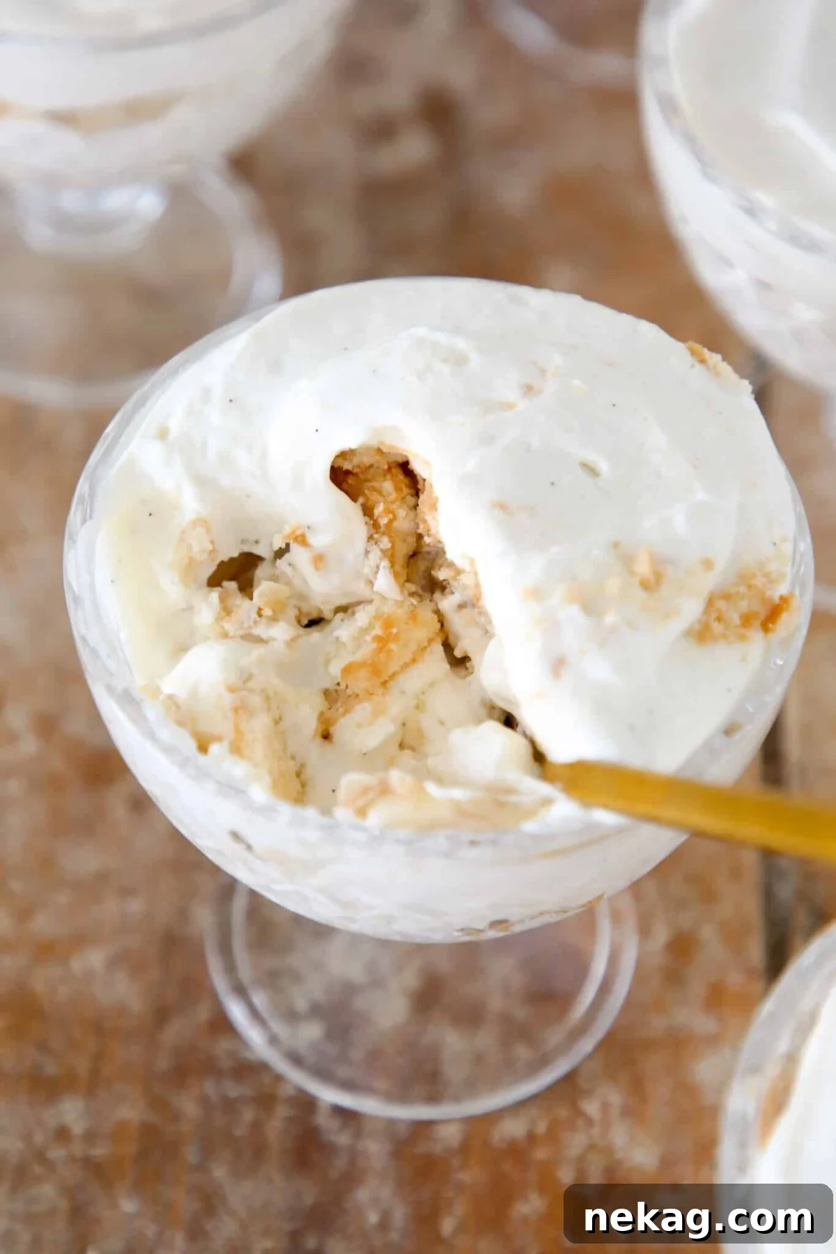 A small glass dish showcasing layers of creamy banana pudding, Nilla wafers, and sliced bananas, with a gold spoon resting beside it, ready to be enjoyed.
