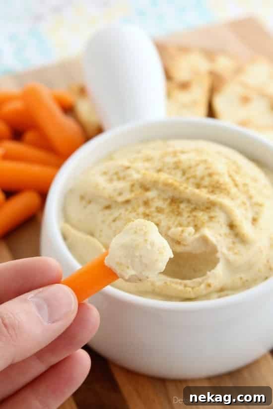 Whip Up Garlicky Hummus 5 Close-up shot of a hand dipping a fresh, crisp carrot stick into a creamy bowl of Easy Garlic Hummus, highlighting the perfect texture for a healthy snack.