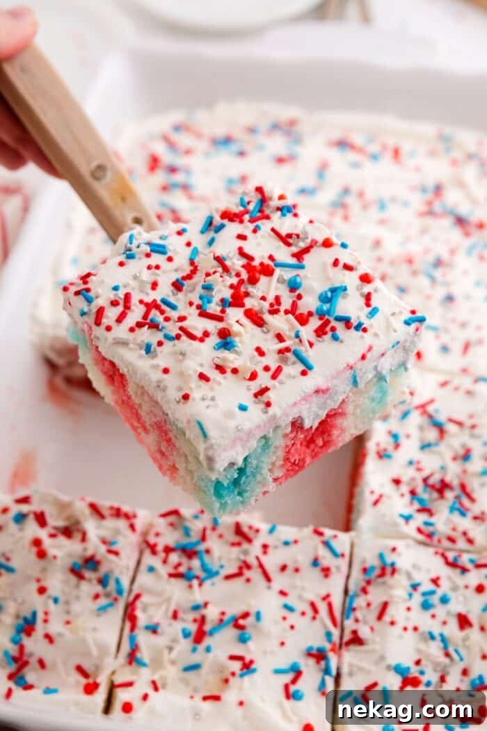 Patriotic poke cake being lifted out of the pan with a spatula.