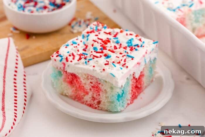 Red white and blue poke cake on a plate with Cool Whip and patriotic sprinkles on top.