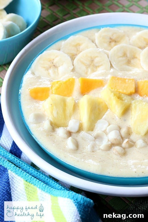 A beautifully arranged tropical smoothie bowl, garnished with fresh fruit slices, macadamia nuts, and chia seeds.
