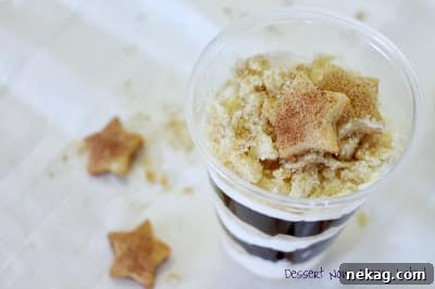 Deconstructed Blueberry Pie Parfaits 3 Close-up side view of a layered parfait with crushed pie crust at the bottom, a creamy white layer, and a vibrant blueberry layer. A small, star-shaped pie crust piece is used as a garnish on top.
