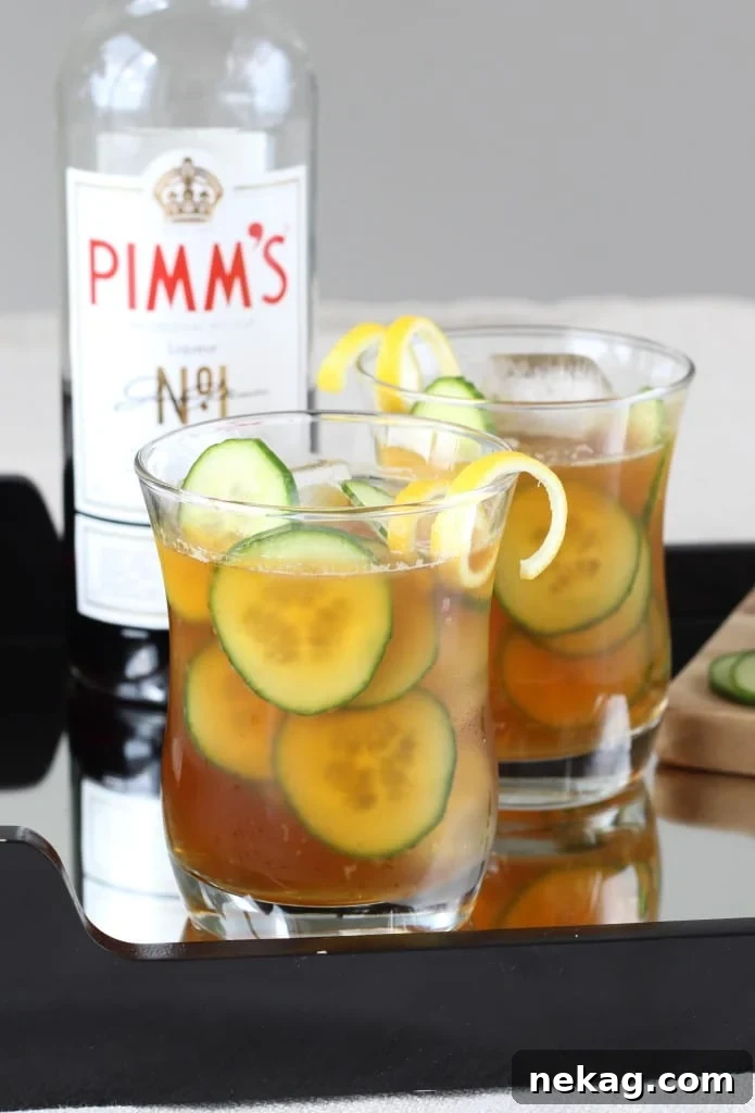 A tall glass of refreshing Cucumber Pimm's Cup, garnished with a lemon twist and cucumber slices, sitting on a wooden surface.