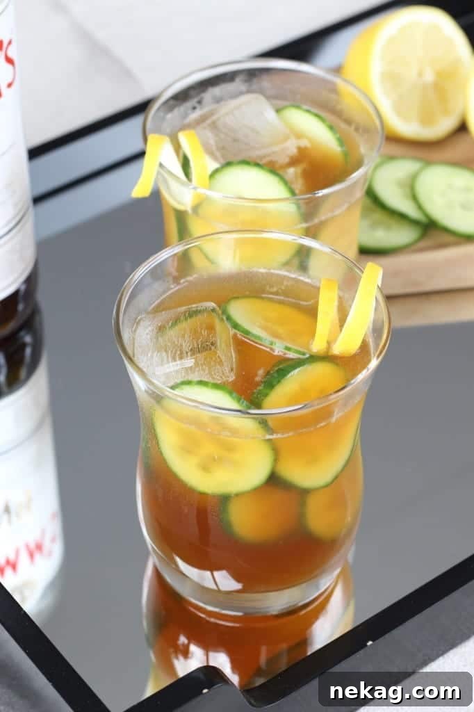 A close-up shot of a single Pimm's Cup, filled with ice and fresh garnishes, against a blurred background.