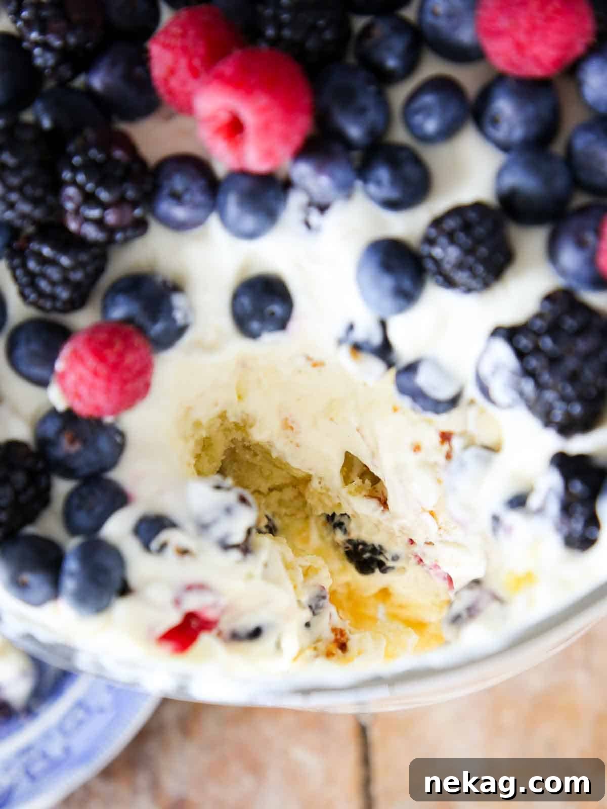 Top view of a trifle dish generously loaded with fresh berries, with a scoop taken out.