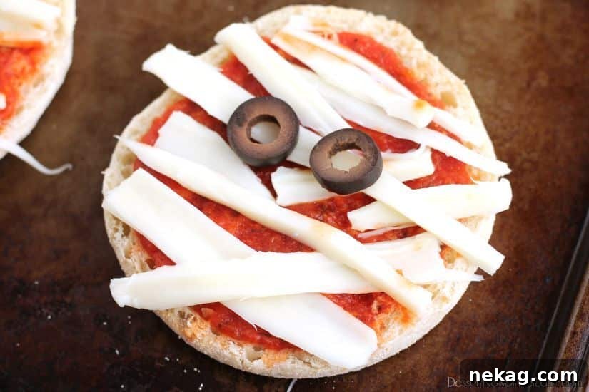 Spooky Swaddle Pizzettes 3 Three Mini Mummy Pizzas on a baking sheet, showcasing creative olive eyes.