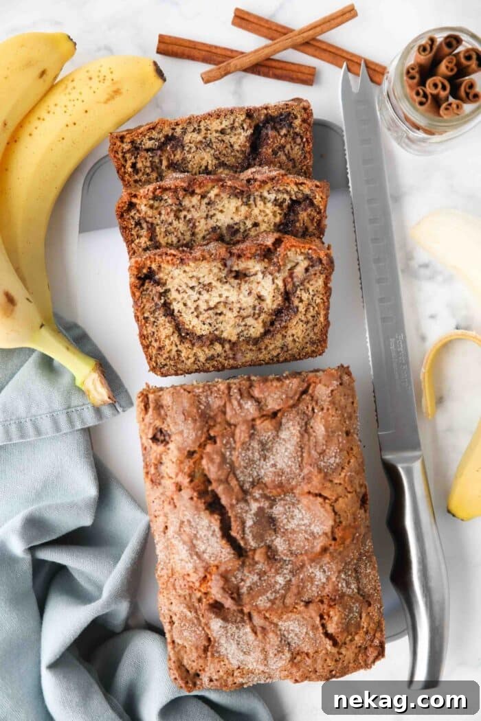 A freshly baked loaf of cinnamon swirl banana bread, with several slices already cut, revealing the tempting layered cinnamon sugar swirl running through the center of the soft, golden-brown bread.