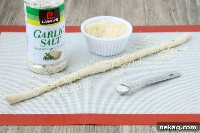 Dough rolled into a stick with parmesan and garlic salt adhering to the outside, ready for shaping.