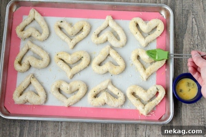Brushing egg wash onto heart shaped breadsticks before baking for a golden finish.