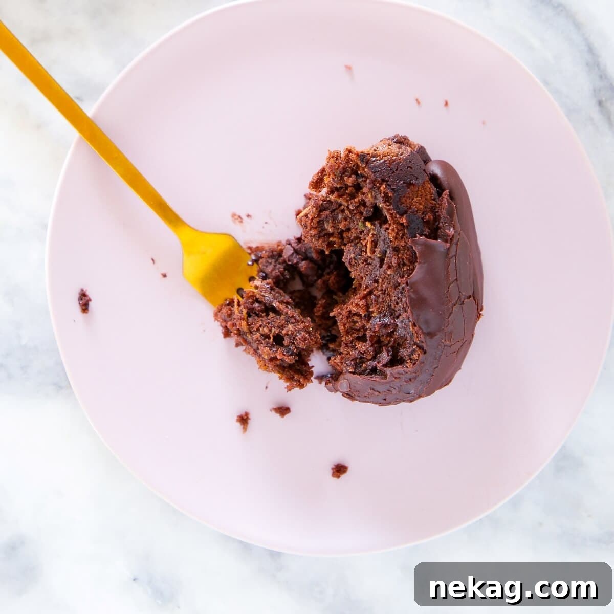 A delectable slice of chocolate zucchini cake being lifted from a plate with a gold fork, showcasing its moist texture.