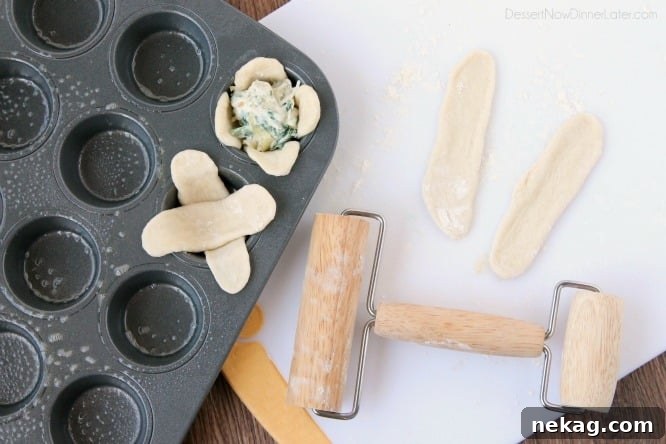 Artichoke Spinach Blossom Bites 8 A mini rolling pin next to two logs of dough rolled flat. A mini muffin pan with two pieces of flattened criss-crossed dough in one cup. Artichoke dip inside another cup of criss-crossed dough.