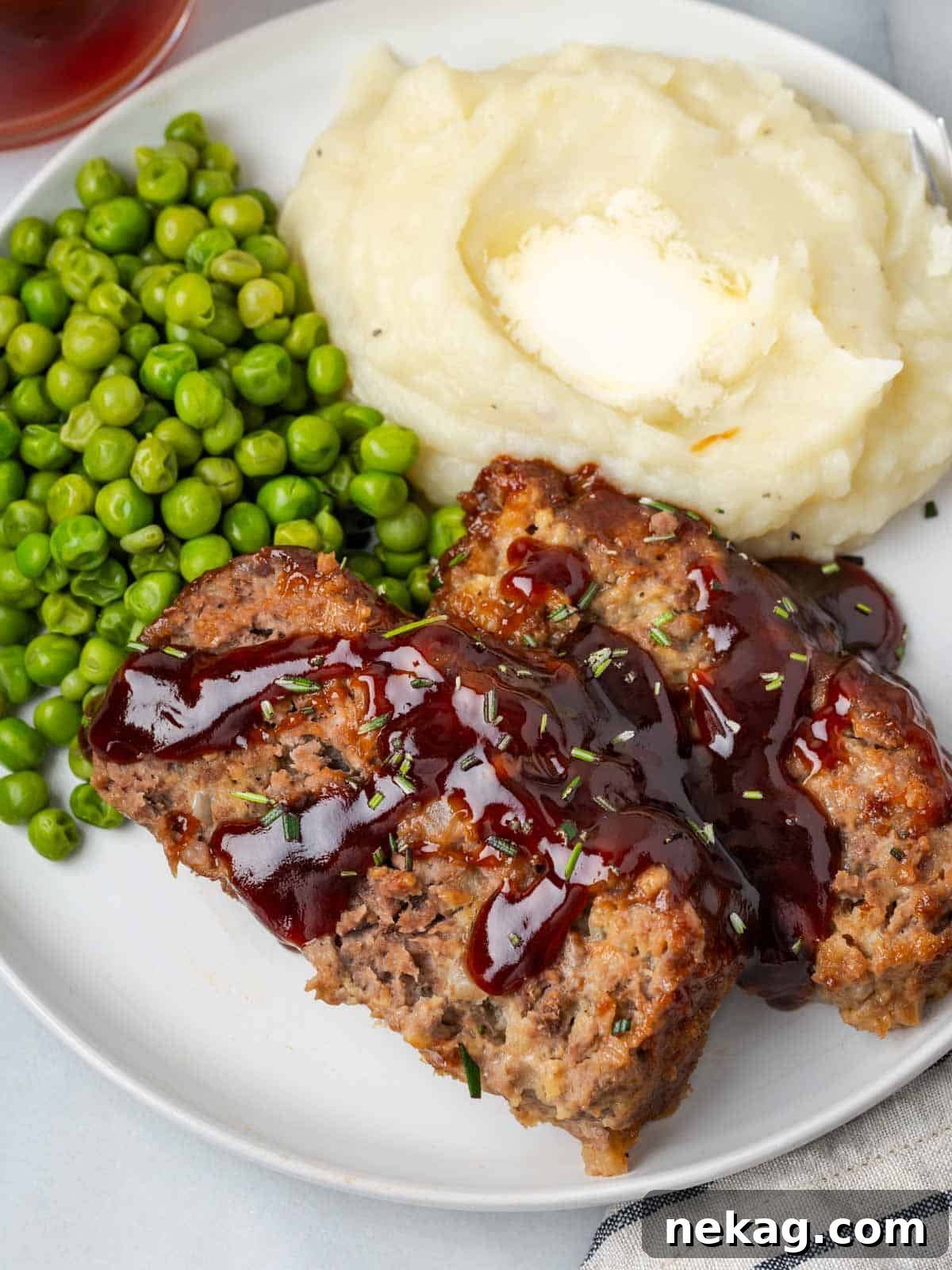 Sweet and Sticky Brown Sugar Meatloaf 2 brown sugar meatloaf sliced on plate with potatoes & peas.