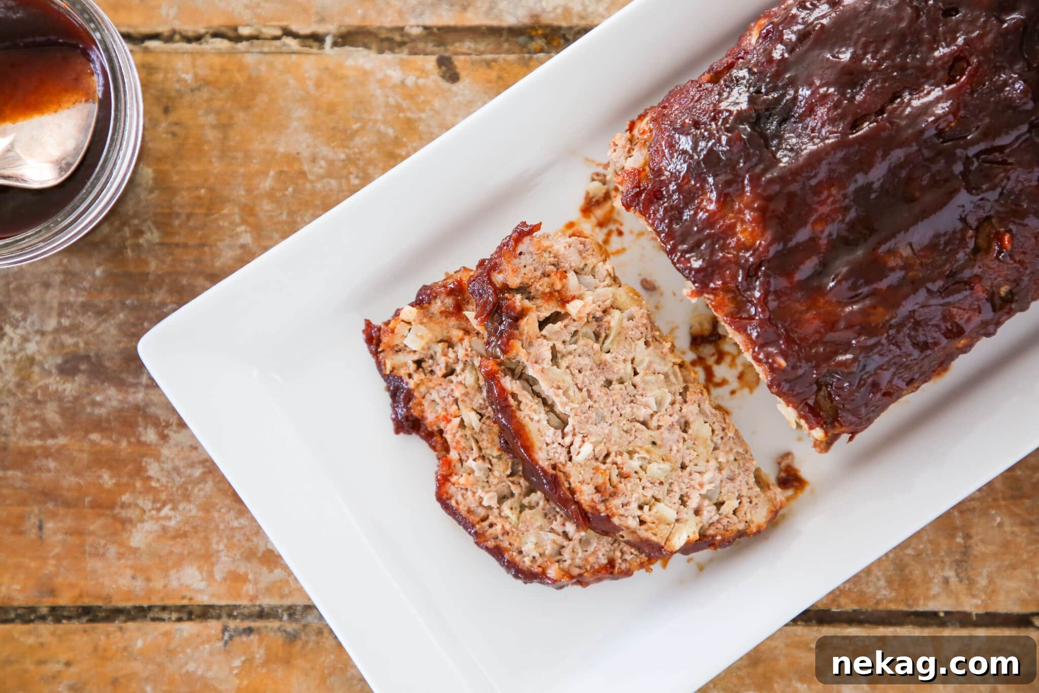 Sweet and Sticky Brown Sugar Meatloaf 9 Meatloaf with two slices sliced off over a white plate on a wood slate background.