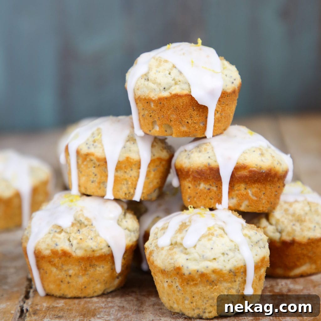 A stack of Lemon Poppyseed Muffins, glazed and ready to be served, with lemons in the background.