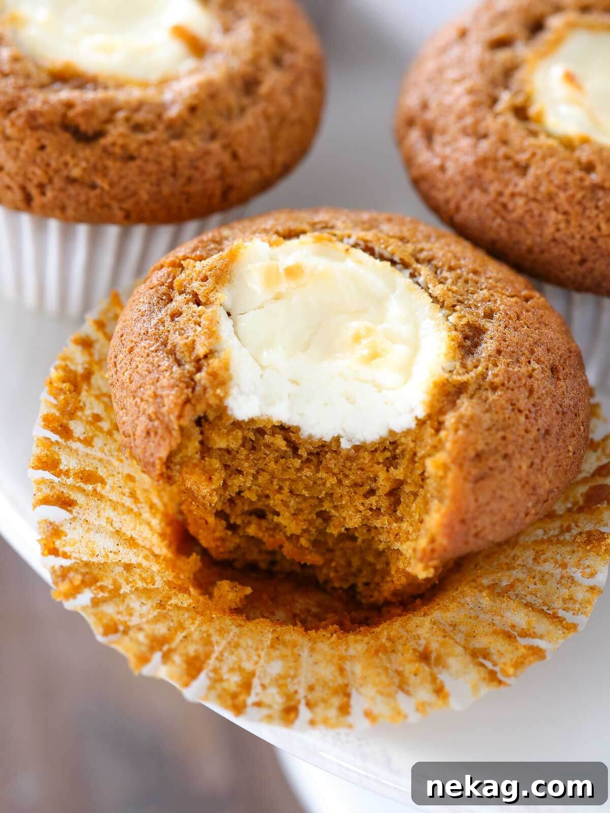 Pumpkin Cheesecake Swirl Muffins 2 A freshly baked pumpkin cream cheese muffin, unwrapped and ready to eat, resting on a cake stand.