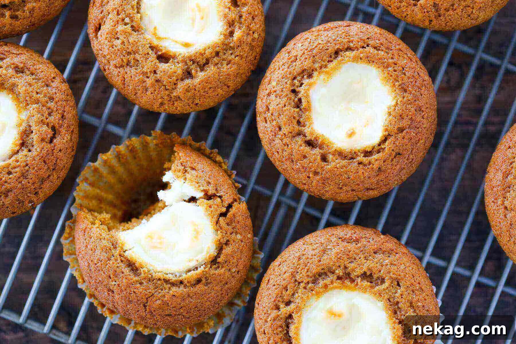 Pumpkin Cheesecake Swirl Muffins 4 Freshly baked pumpkin muffins with visible cream cheese filling cooling on a wire rack.