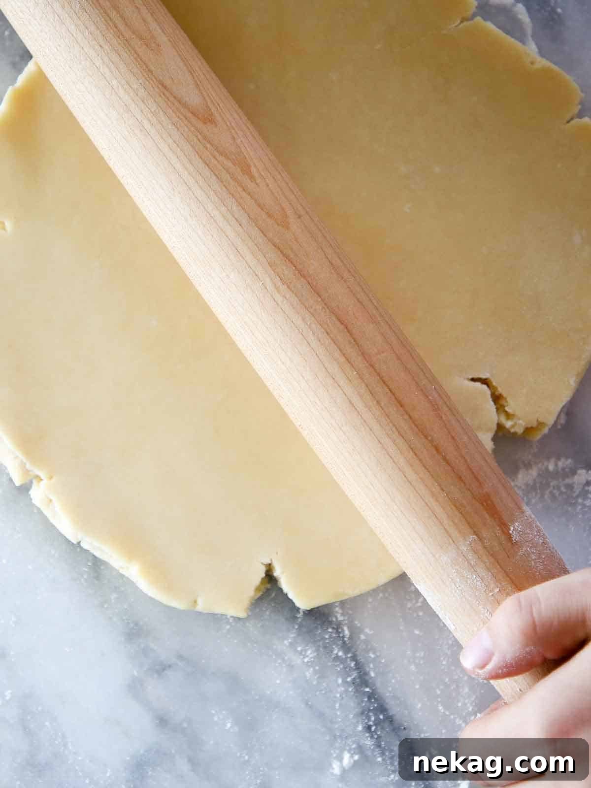 Pâte Sucrée dough disk being rolled by wooden pin on marble. A step in creating the perfect sweet tart crust.