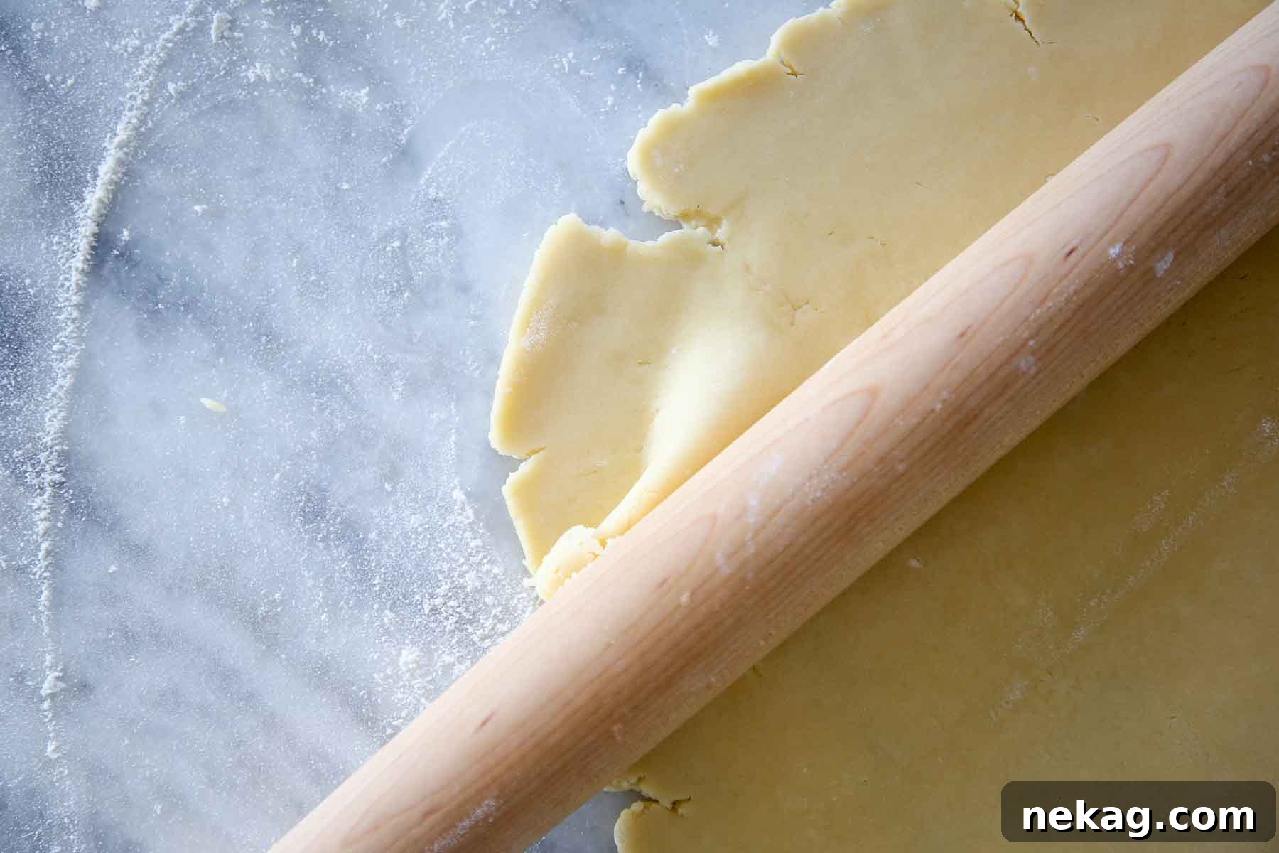 Pâte Sucrée dough disk being rolled thin by wooden pin on marble, illustrating the ease of preparation.
