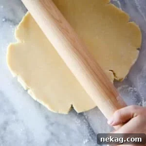 Pâte Sucrée dough disk being rolled by wooden pin on marble.