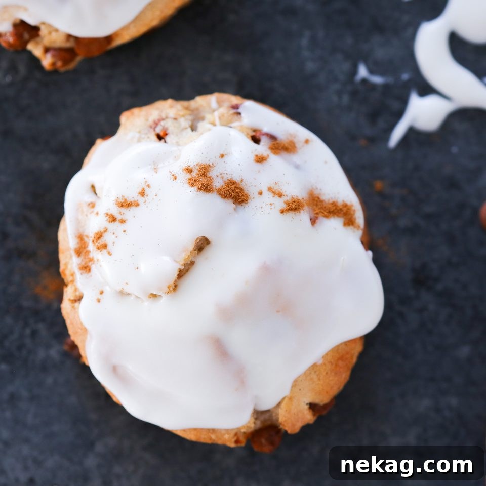 Sweet Cinnamon Swirl Scones 4 A perfectly glazed cinnamon scone sits on a baking rack, showing off its rich cream cheese topping and inviting texture.