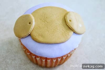 Two small brown fondant circles placed at the top sides of the muzzle, forming the ears.