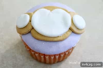 White fondant shapes (two small circles and one medium with a 'v' cut) adhered to the brown muzzle to form the face details.