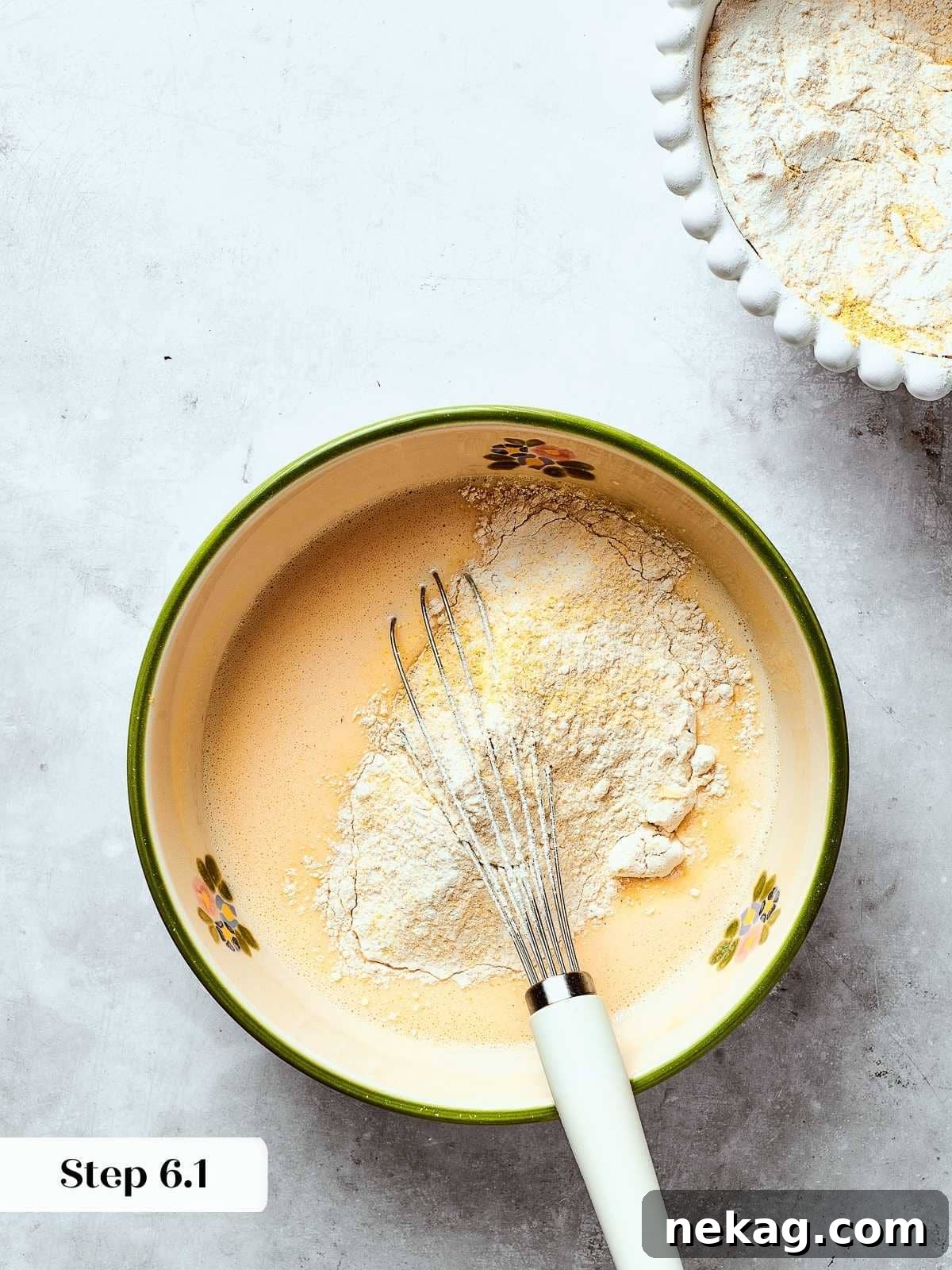 Dry ingredients being added to wet mixture while whisking to form a smooth cornbread batter.