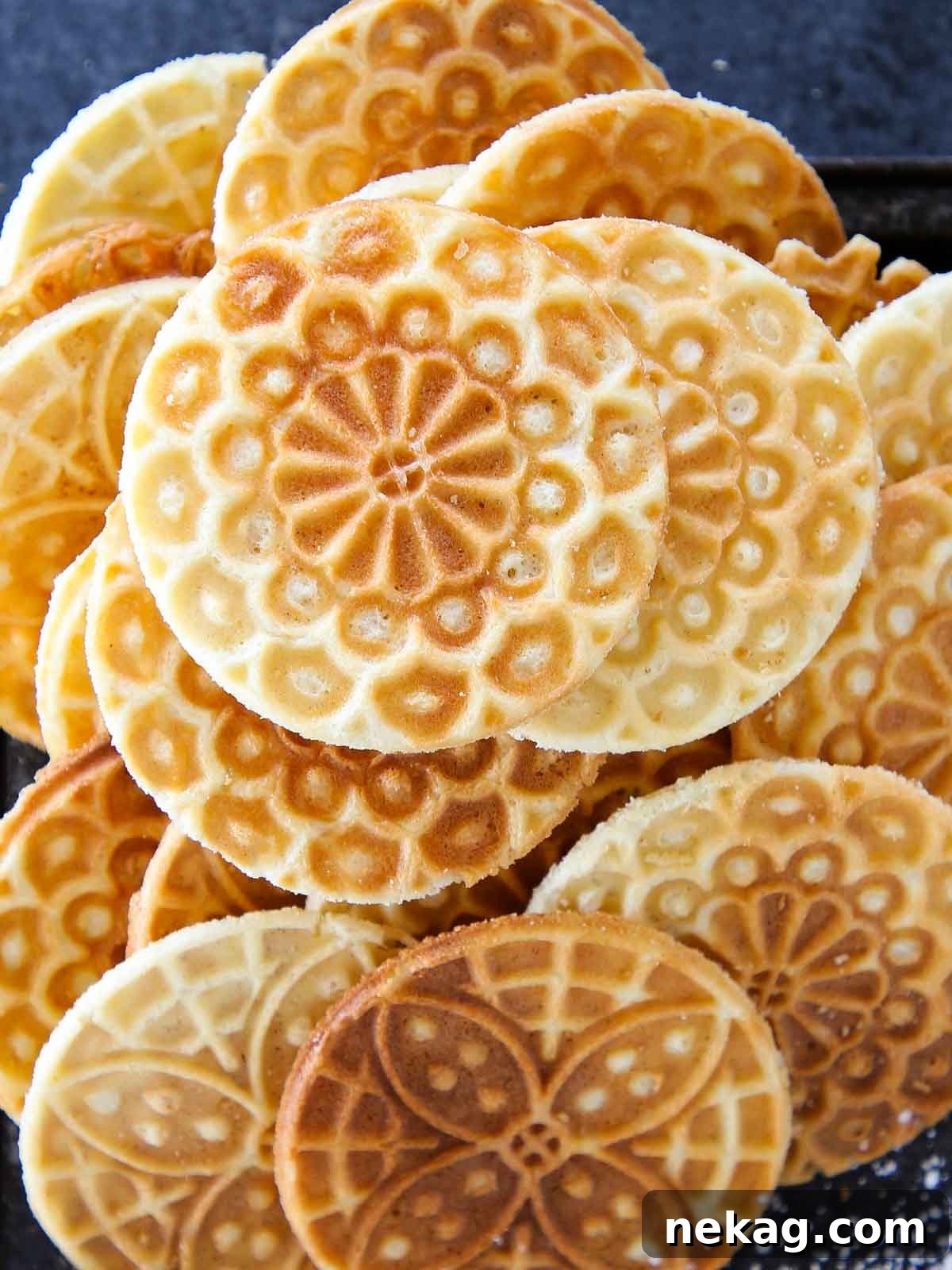 Pizzelle cookies piled artfully on a black tray, showcasing their intricate snowflake-like patterns.