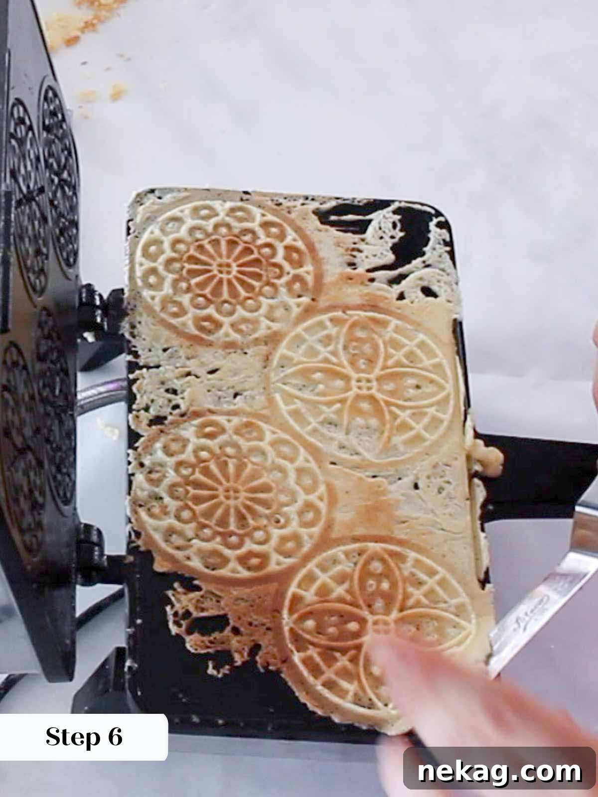 Golden brown pizzelles being gently removed from the open pizzelle iron.