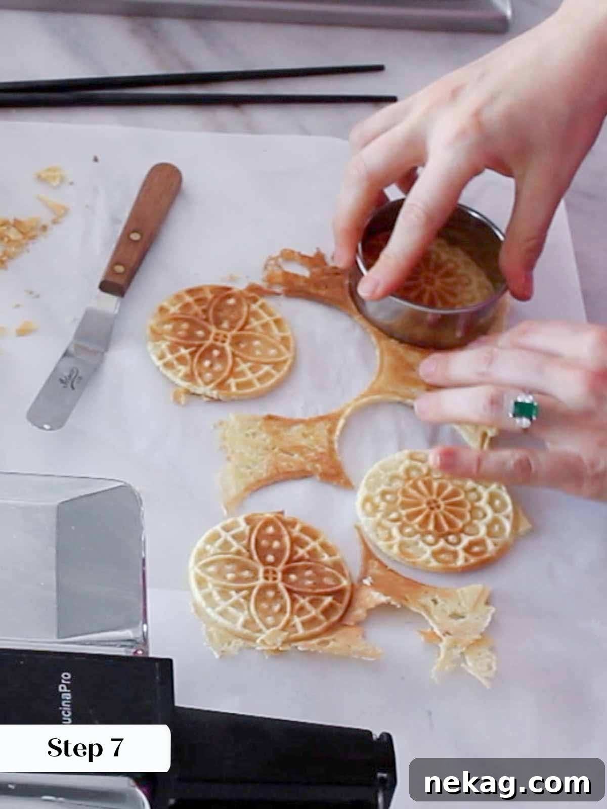 A person using a round cookie cutter to trim the edges of warm pizzelle cookies.