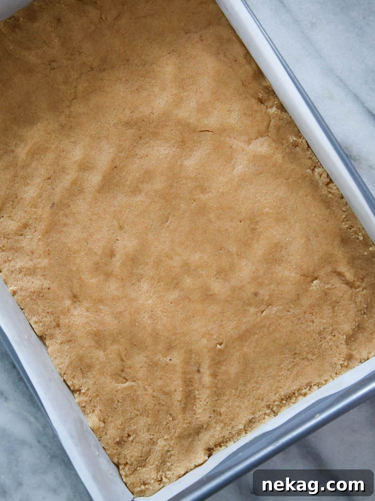 Irresistible Almond Bars 5 Cookie dough evenly pressed into the bottom of a silver baking pan, ready for the topping.