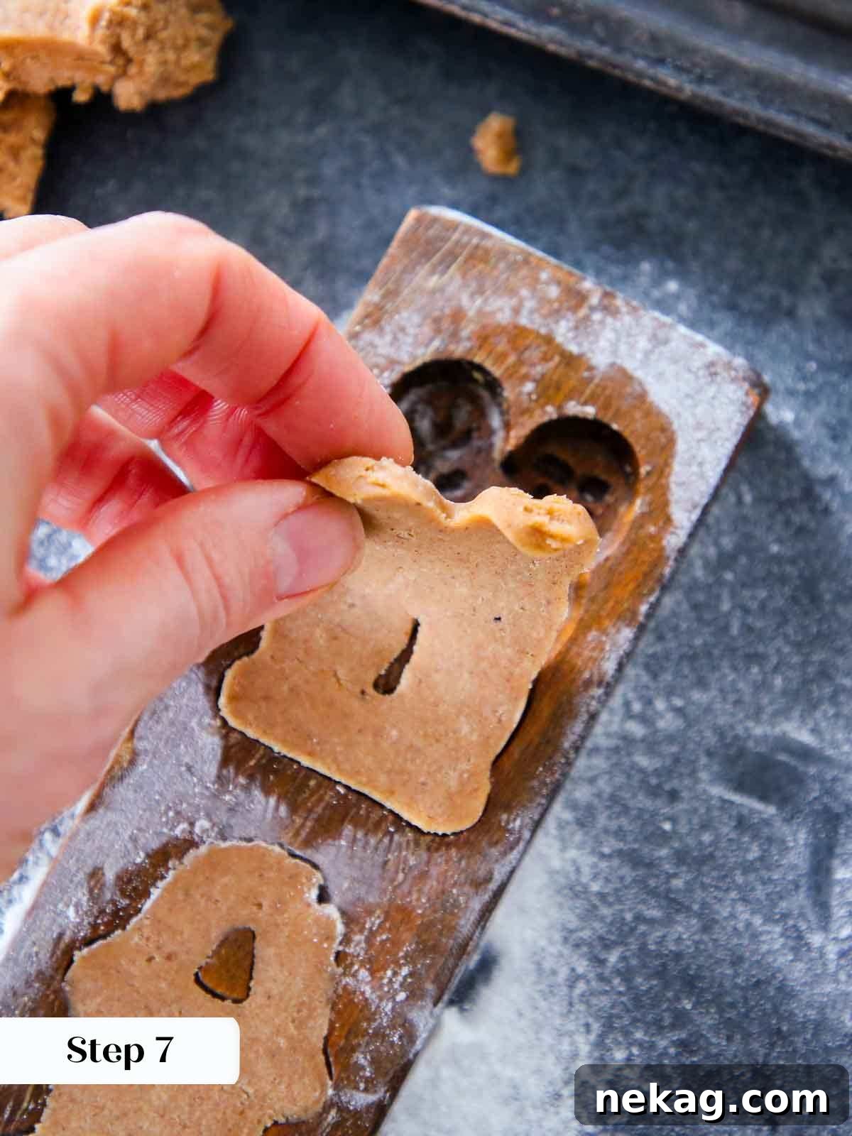 Carefully peeling a molded Speculoos cookie from a wooden mold, revealing its intricate design.