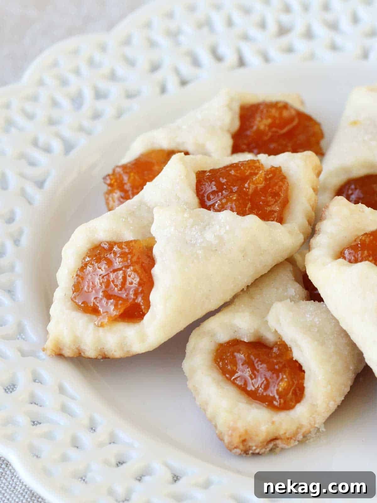 Apricot Kolacky Cookies stacked on a white lace plate, highlighting their delicate pastry and fruit filling.